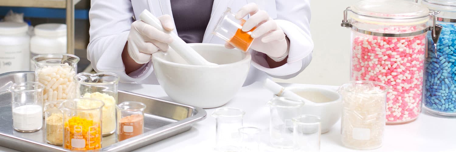 Eine Apothekerin stellt mit Mörser und verschiedenen Wirkstoffen eine individuelle Arzneimittelrezeptur her.
